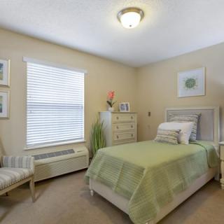 A cozy bedroom with a single bed featuring green bedding and simple, elegant decor.