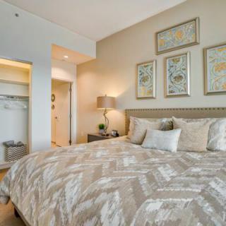 A well-decorated bedroom with neutral tones, featuring a comfortable bed, stylish lamp, and framed artwork on the wall.