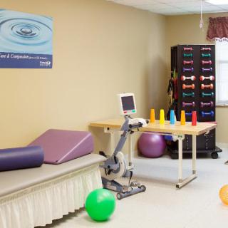 A physical therapy room equipped with exercise equipment, including mats, fitness balls, cones, and weights.