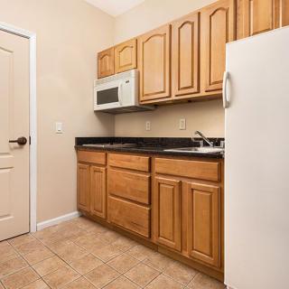 A compact kitchen with wooden cabinets, a microwave, refrigerator, and a sink.