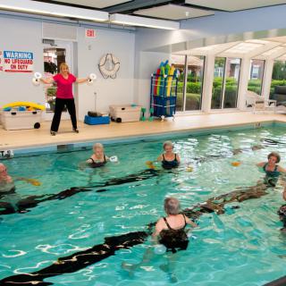 A group of seniors participating in an aquatic exercise class led by an instructor in an indoor swimming pool.
