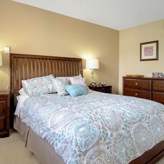 A cozy bedroom featuring a neatly made bed with patterned bedding, bedside tables with lamps, and a dresser.