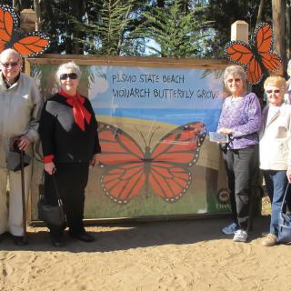 A group of people standing in front of a butterfly sanctuary sign outdoors.