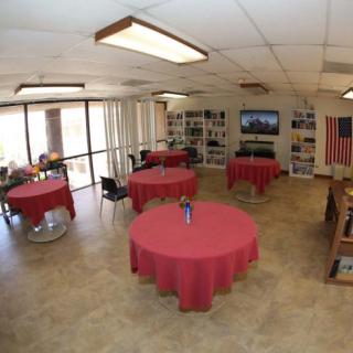 A spacious indoor event area featuring tables with red tablecloths, chairs, a flag, and a television.