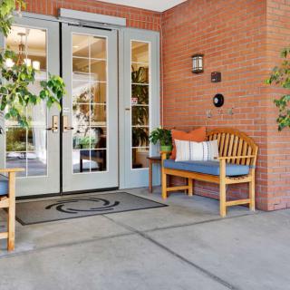A welcoming entrance with a wooden bench and greenery beside glass double doors.