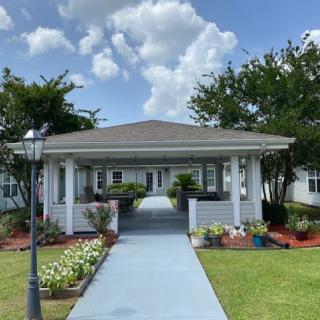 A charming house with a pathway surrounded by flowers and trees under a cloudy sky.