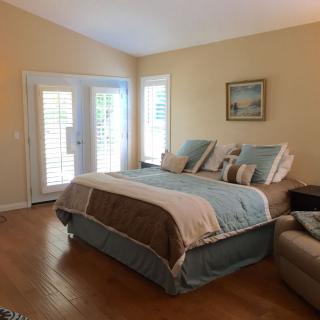 A cozy bedroom with a neatly made bed, warm lighting, and sunlight streaming through the windows.