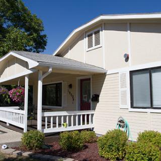 A charming two-story house with a welcoming front porch and well-maintained landscaping under a clear blue sky.