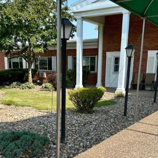 A well-maintained entrance leading to a brick building, surrounded by greenery and decorative lampposts.
