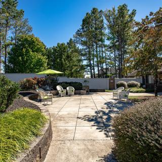 A spacious backyard with patio seating, surrounded by trees and garden landscaping under a clear blue sky.