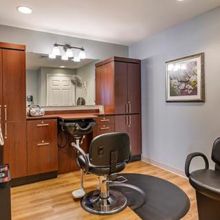 An interior view of a barber shop with a styling chair, mirrors, and cabinets.