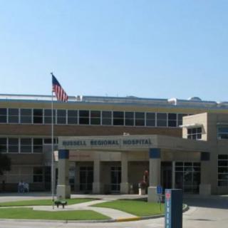 The exterior of a hospital building with an entrance and an American flag displayed.