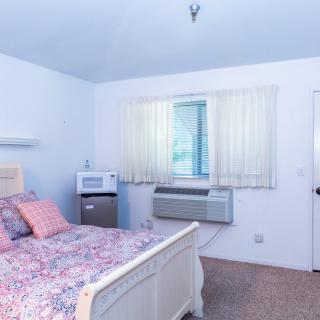 A cozy bedroom with a bed, air conditioner, and microwave.