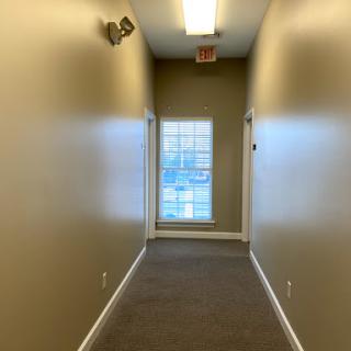 A view down a well-lit hallway with beige walls and a window at the end.
