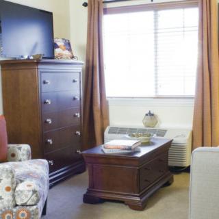 A cozy living room with a dresser, coffee table, and TV near a window covered by curtains.