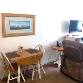 A cozy living space featuring a small dining table with chairs, a painting on the wall, and a TV setup next to an armchair.