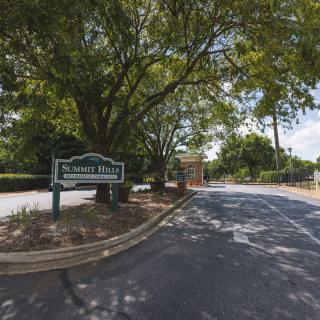 Entrance to a park with a road lined by trees and a welcoming sign.