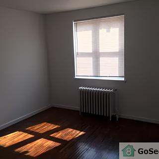 An empty room with sunlight streaming through a window onto hardwood floors.