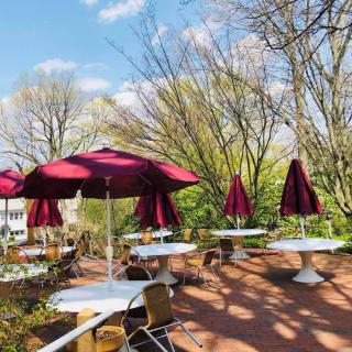 A picturesque outdoor patio with tables and chairs under red umbrellas, surrounded by lush trees.