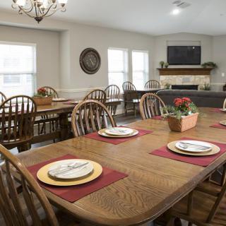 A spacious dining room with wooden tables and chairs, set with plates and red placemats, featuring a chandelier and a fireplace.