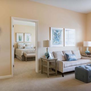 A cozy living room with neutral tones, featuring a sofa and a view into the bedroom.