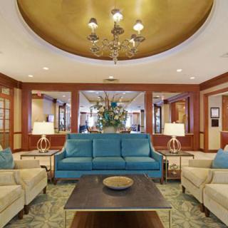Elegant living room with a central blue sofa, surrounded by beige chairs and illuminated by a chandelier.