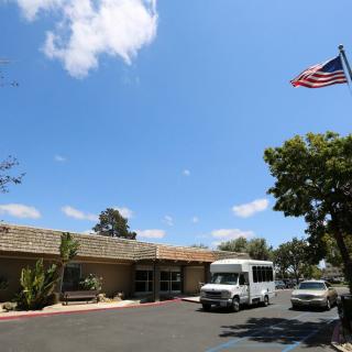 A sunny day outside a building with an American flag, trees, and parked vans.