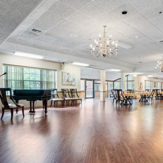A spacious ballroom with a grand piano and chandeliers, featuring wooden floors and large windows.