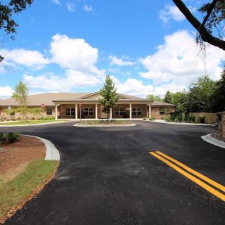A large building with a driveway surrounded by trees under a blue sky with clouds.