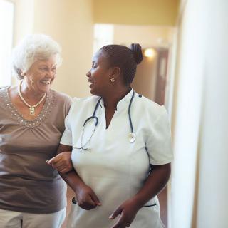 A nurse assists an elderly woman while walking down a hallway.