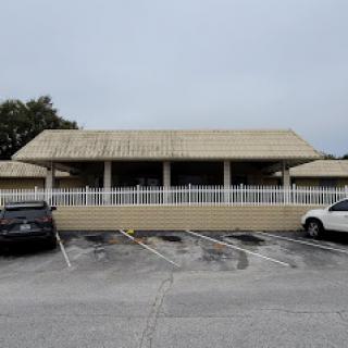 A restaurant building with a covered porch, surrounded by parked cars on a cloudy day.