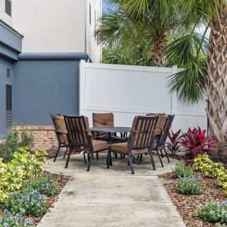 A cozy outdoor patio area with a set of chairs and a table surrounded by lush plants and palm trees.