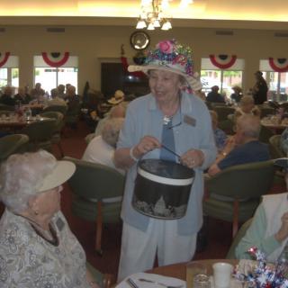 An elderly woman wearing a colorful hat engages with others at a social gathering.