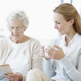 A young woman enjoying a conversation with an elderly lady who is reading.
