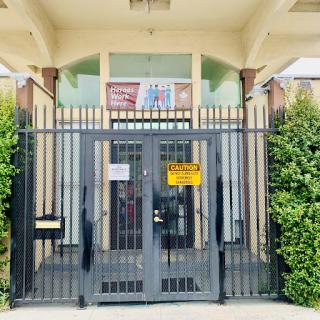 The entrance of a building secured by a gated fence, surrounded by lush greenery.
