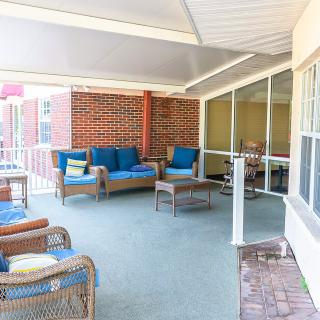 A cozy covered patio with wicker furniture and blue cushions, adjacent to a large windowed wall.