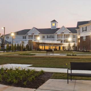 A beautifully lit building at dusk with a landscaped garden and benches in the foreground.