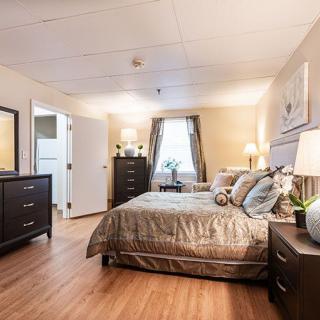 A cozy and well-decorated bedroom with hardwood flooring, featuring a comfortable bed, multiple dressers, and stylish lamps.