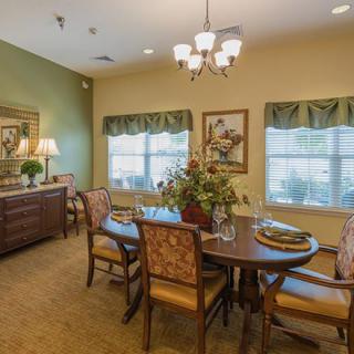A cozy dining room featuring a table set with elegant chairs, a chandelier overhead, and warm decor including artwork and a lamp.