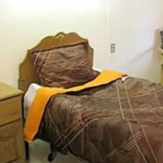 A simple bedroom setup featuring a single bed with brown bedding and an orange blanket.