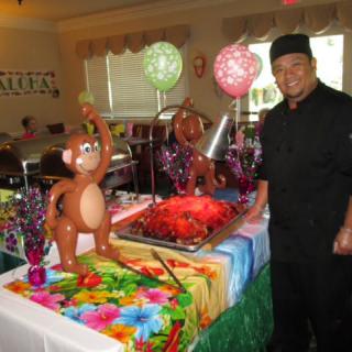 A chef stands beside a colorful buffet table with a balloon monkey and festive decorations.