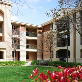 A view of a residential apartment building with manicured landscaping, featuring blooming flowers and green grass.