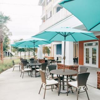 A row of tables and chairs with teal umbrellas on an outdoor restaurant patio.