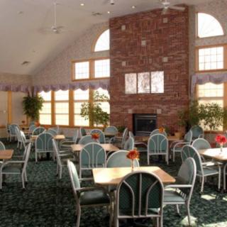 A spacious dining area with multiple tables and chairs, a brick fireplace, and large windows.