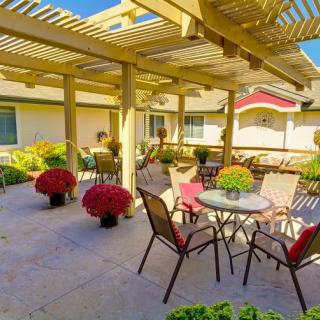 A cozy outdoor patio with a pergola, featuring tables and chairs surrounded by vibrant flower pots under a sunny sky.