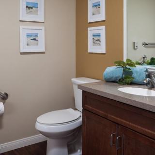 A neatly organized bathroom with a toilet, sink, and mirror, featuring decorative elements such as framed artwork and rolled towels.