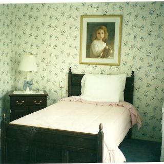 A cozy bedroom with a single bed, floral wallpaper, and a portrait hanging above the bed.