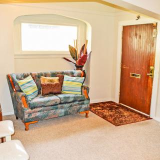 A cozy living room with a patterned sofa, decorative pillows, and an indoor plant near the entrance.