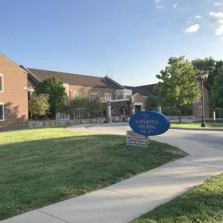Entrance to St. Norbert College with a curved pathway and blue sign.