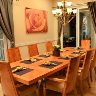 A beautifully set dining room with a large table and elegant chairs, illuminated by a chandelier.